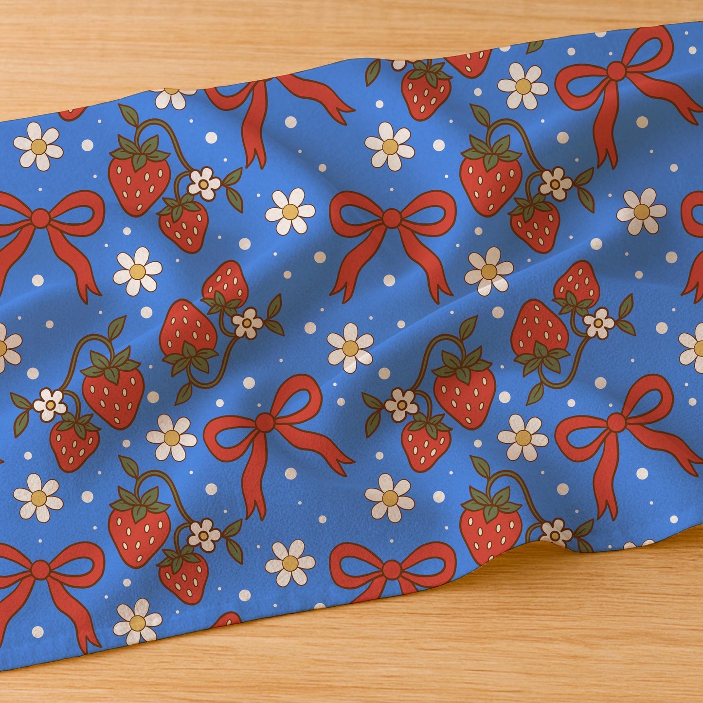 Blue strawberry and bow pattern printed on folded fabric placed on wooden surface.