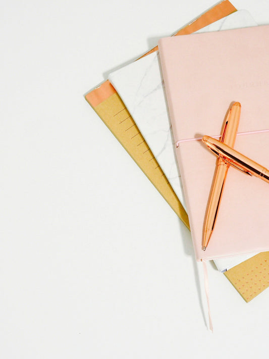 Three notepads on a pale grey background with 2 rose gold pens
