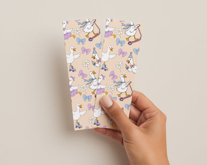 Hand holding a set of patterned bookmarks with cartoon geese and bows on a beige background