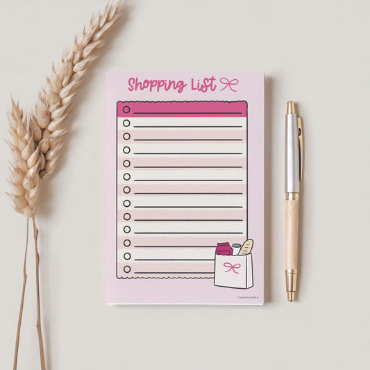 a5 shopping list pink themed. on plain background with pen and plant