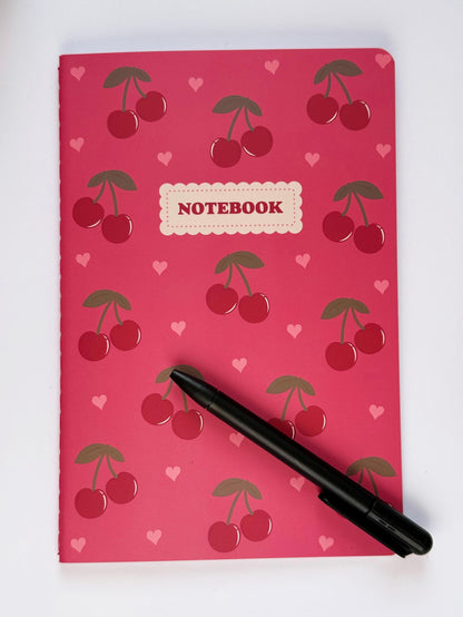 Cherry-pattern notebook with a pen placed on top to show scale and everyday writing use.