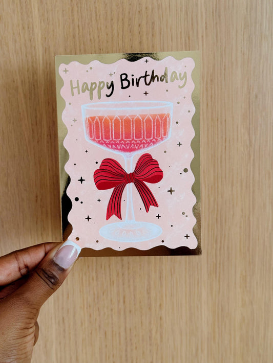 champagne glass with gold foil birthday card in hand
