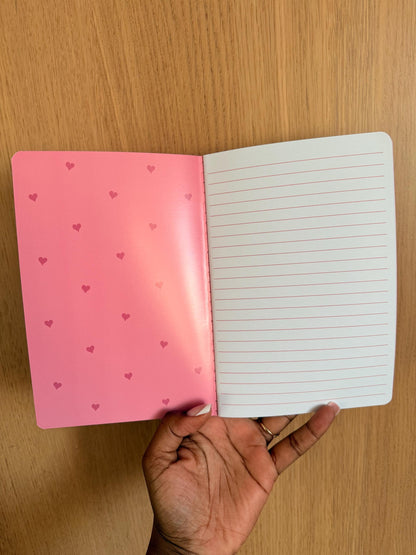 Notebook opened to show lined interior pages with a soft pink inside cover.