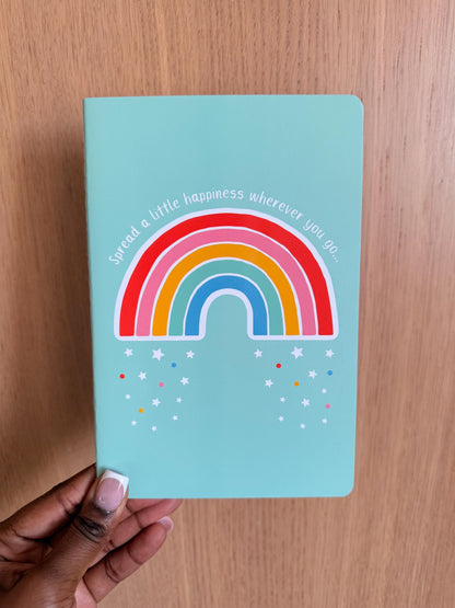 Mint green notebook with a colorful rainbow illustration and the phrase “Spread a little happiness wherever you go” on the cover.