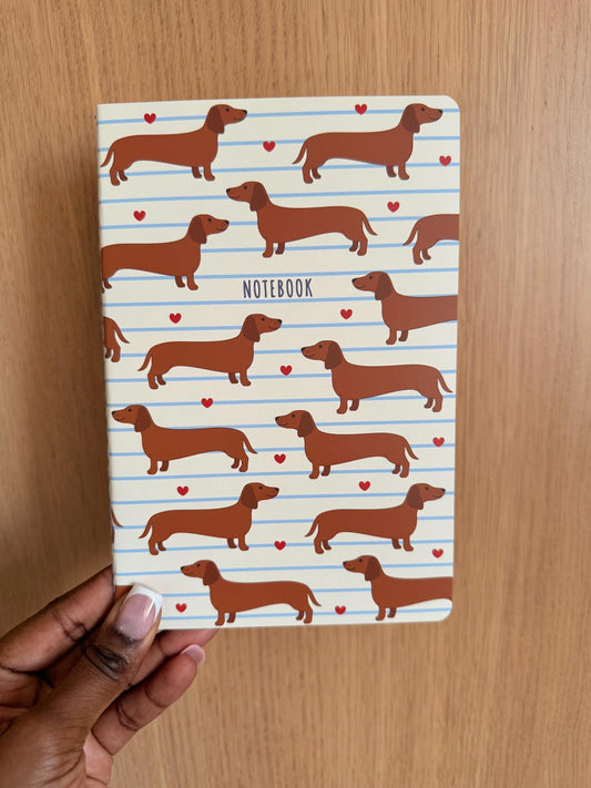 Dachshund-themed notebook with a repeating sausage dog pattern and small heart accents on a lined background.